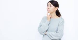 上を向き人差し指を口元にあて、考えている女性
